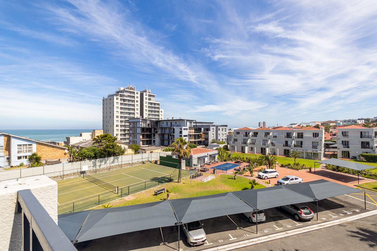 Aerial view of the apartment complex grounds featuring a tennis court, swimming pool, landscaped gardens, and covered parking facilities.