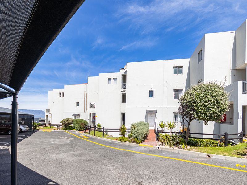 Exterior view of the apartment complex featuring a paved driveway, covered parking bays, and landscaped garden areas.