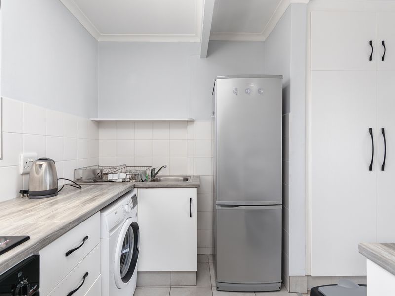 A functional laundry area featuring built-in cabinetry, a stainless steel sink, tiled backsplash, and space for a washing machine.