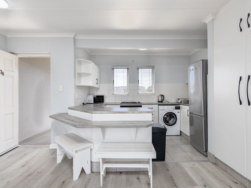 A functional kitchen featuring white cabinetry, laminate countertops with a breakfast bar, tiled backsplash, and integrated laundry facilities in a clean, neutral space.