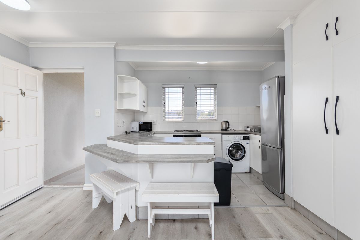 A functional kitchen featuring white cabinetry, laminate countertops with a breakfast bar, tiled backsplash, and integrated laundry facilities in a clean, neutral space.
