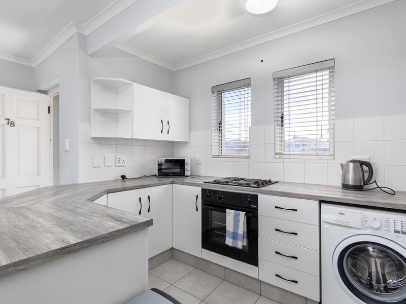 A functional kitchen featuring white cabinetry, wood-look laminate countertops, a built-in oven with hob, and space for a washing machine.