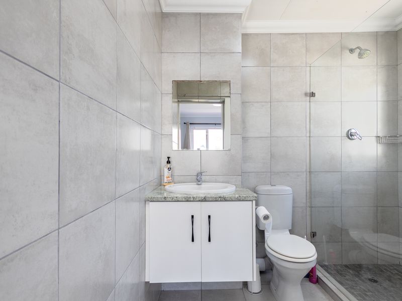 A modern bathroom featuring grey ceramic wall and floor tiles, a vanity with granite countertop, and a glass-enclosed shower.