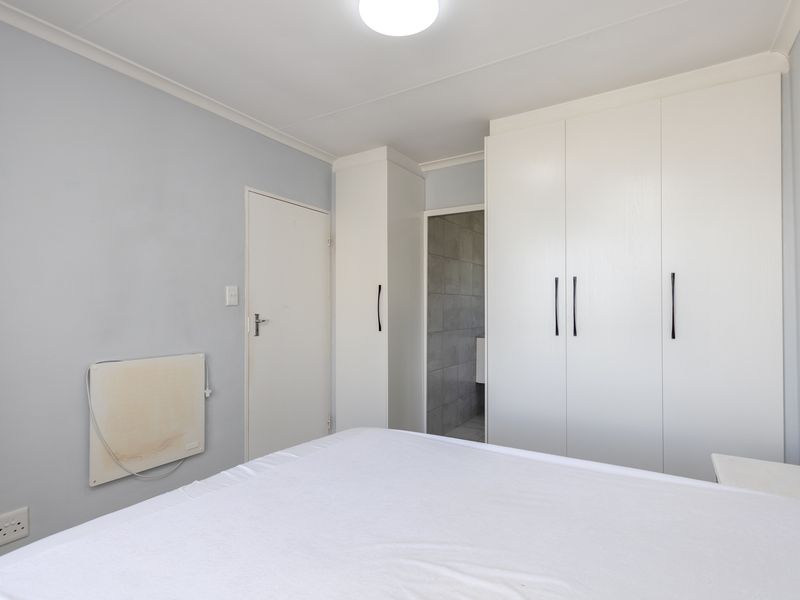 A bedroom featuring built-in white cupboards, neutral wall tones, and direct access to an en-suite bathroom.