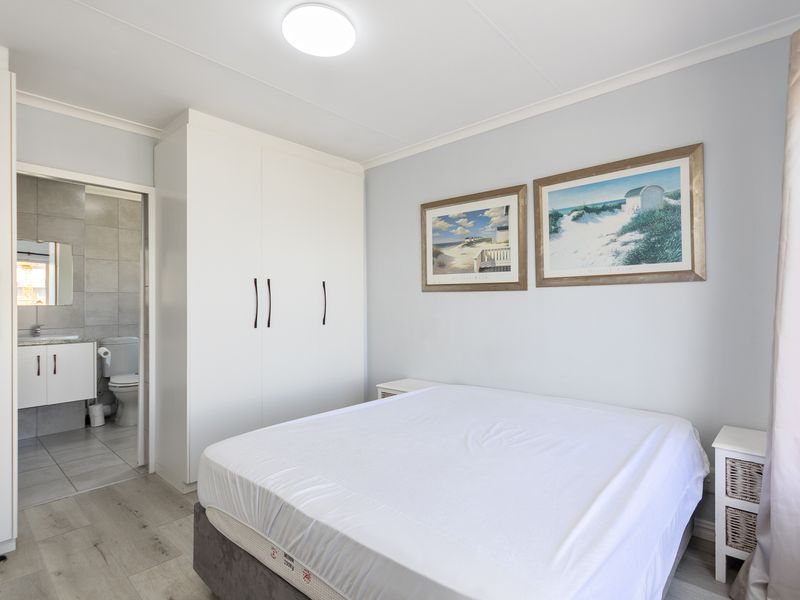 A well-maintained bedroom featuring built-in cupboards, laminate flooring, and direct access to an en-suite bathroom with modern tiling.