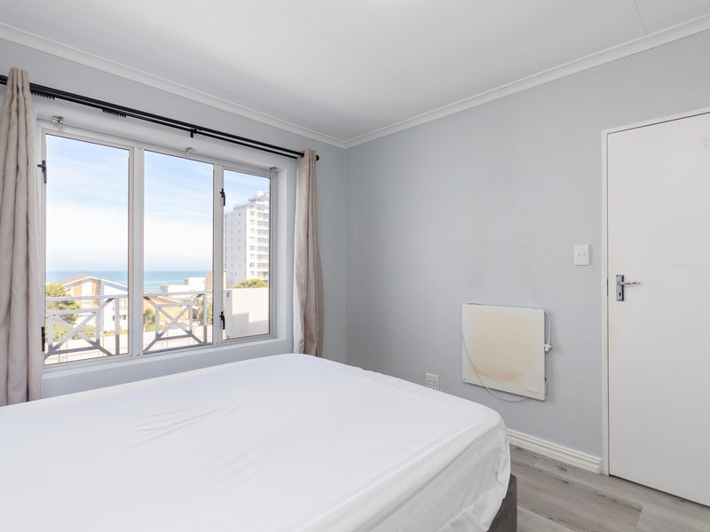 A bright bedroom featuring laminate flooring, cove cornicing, and a window offering coastal views.