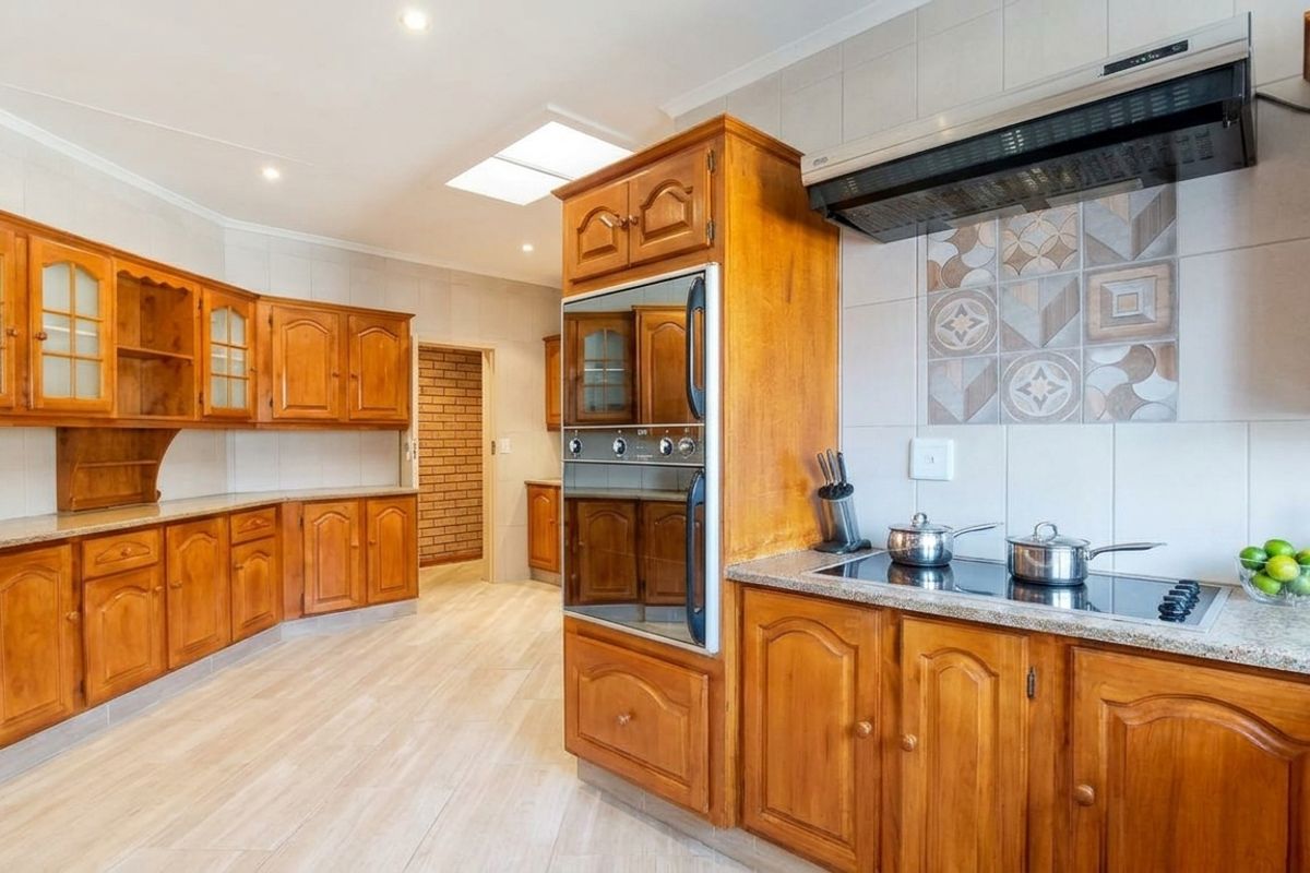 Spacious kitchen featuring traditional wooden cabinetry, granite countertops, built-in double oven, electric hob, and a skylight for natural illumination.
