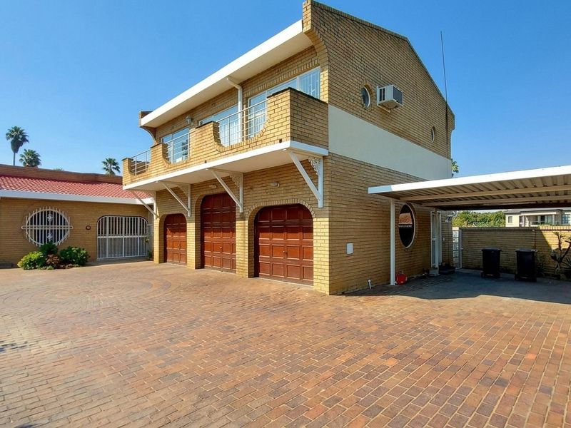 Front exterior view of a multi-level brick house featuring a paved driveway, triple garage, attached carport, and an upper-level balcony.