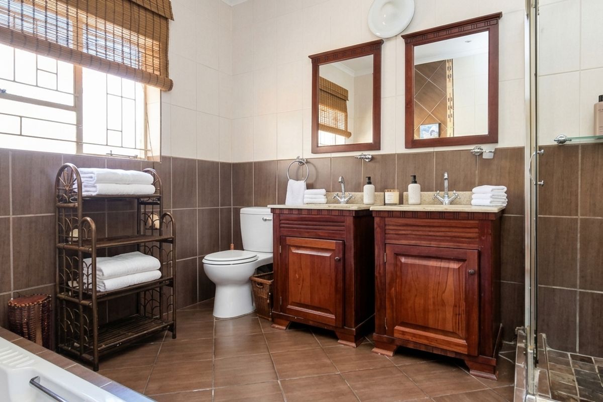 A well-appointed bathroom featuring a double vanity with wooden cabinetry, a separate shower enclosure, a bathtub, and neutral wall and floor tiling.