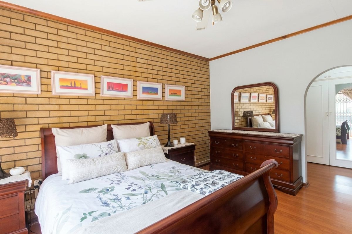 A spacious bedroom featuring an exposed brick feature wall, laminate flooring, and an arched doorway leading to an adjacent area.