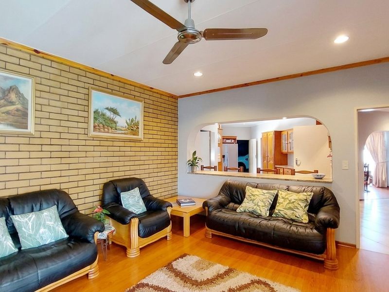 A living room featuring an exposed brick feature wall, ceiling fan, and a convenient pass-through window connecting to the kitchen area.