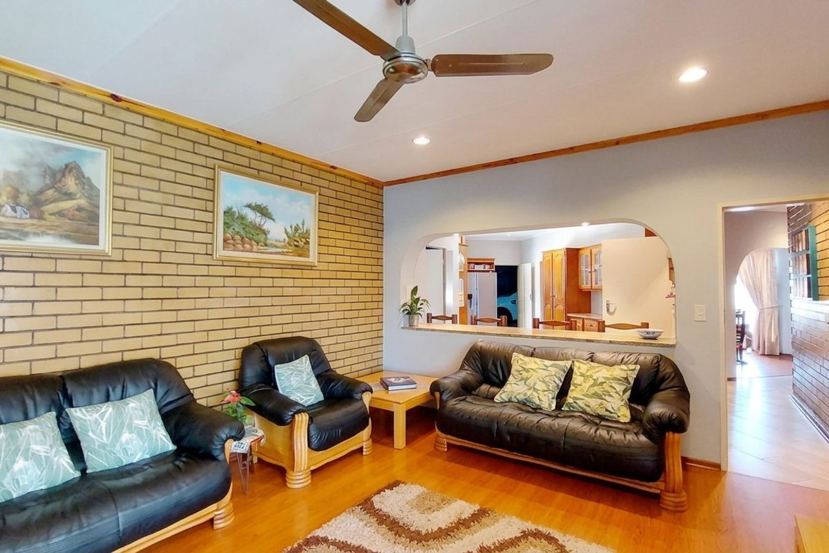 A living room featuring an exposed brick feature wall, ceiling fan, and a convenient pass-through window connecting to the kitchen area.
