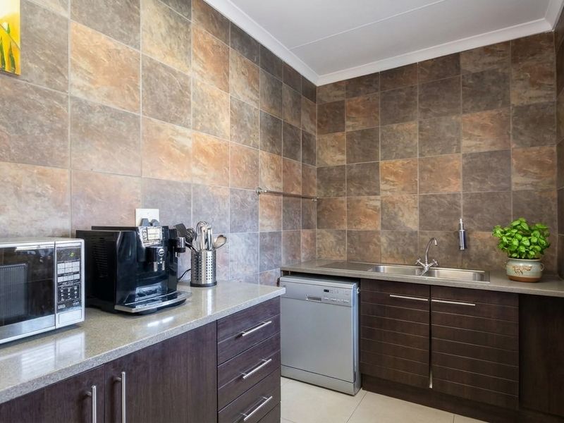 A functional scullery featuring dark wood cabinetry, stone countertops, a stainless steel sink, and full-height tiled wall finishes.