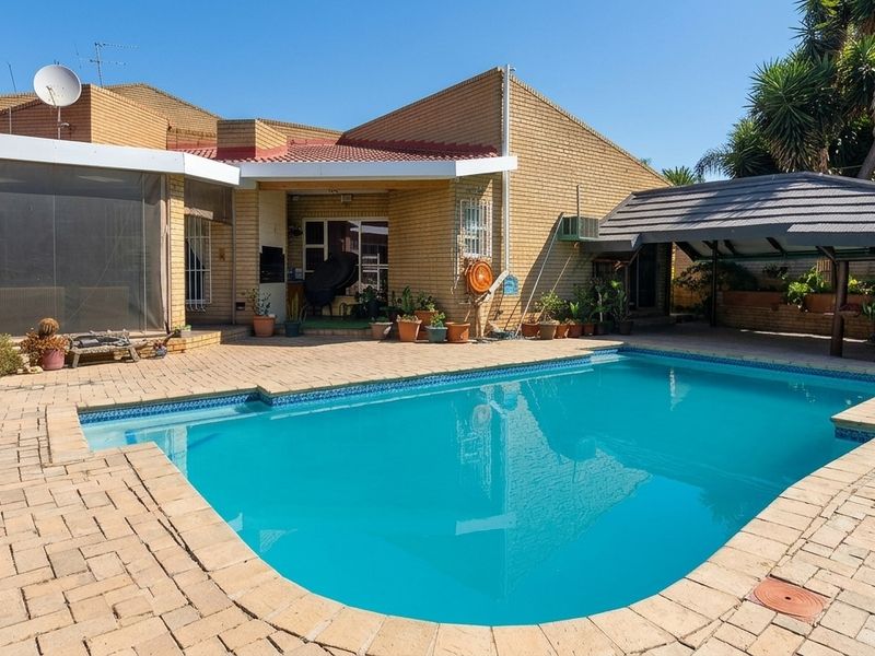 A well-maintained outdoor pool area featuring a paved patio, covered entertainment space, and a built-in braai, perfect for outdoor living and relaxation.