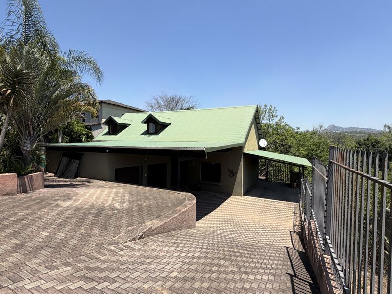 Front exterior view of the property featuring a paved driveway, corrugated metal roof with dormer windows, and perimeter security fencing.