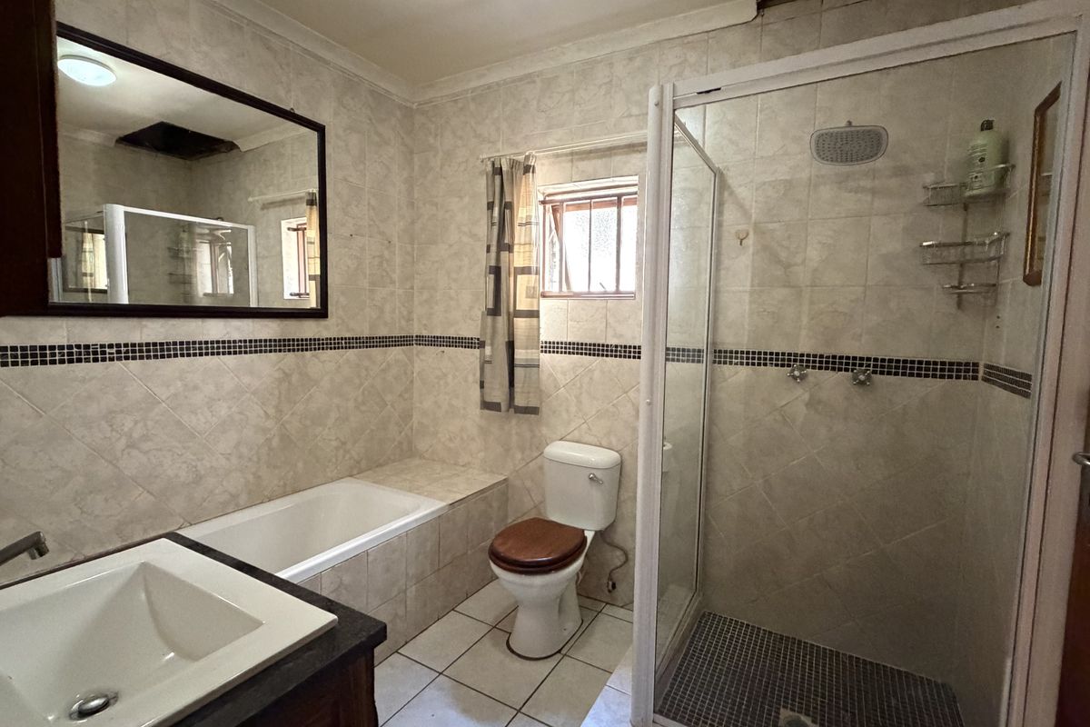 A functional bathroom featuring a built-in bathtub, separate shower enclosure, toilet, and vanity basin with tiled finishes throughout.