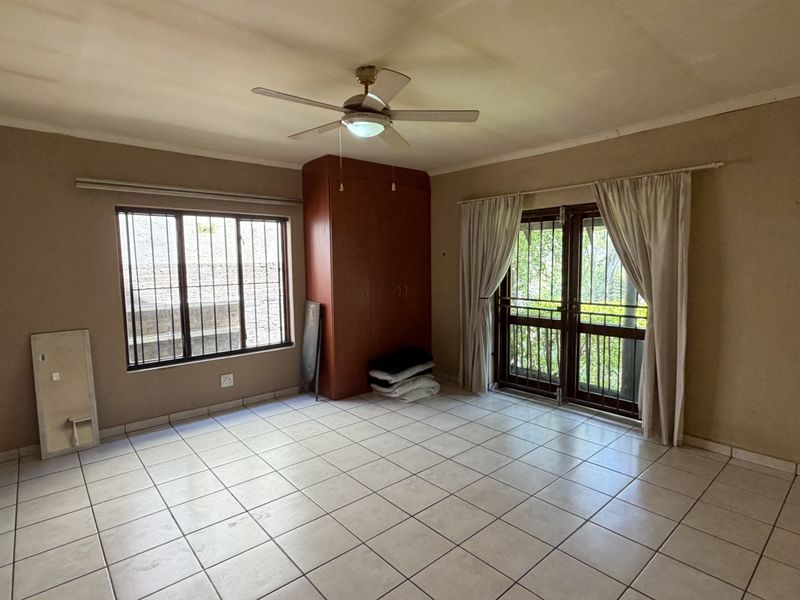 Spacious bedroom featuring tiled flooring, built-in cupboards, a ceiling fan, and direct access to the exterior through a secure door.