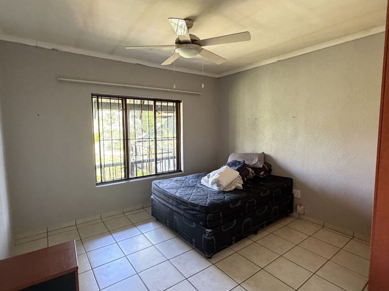 A bedroom featuring tiled flooring, a ceiling fan, and a window fitted with security bars.
