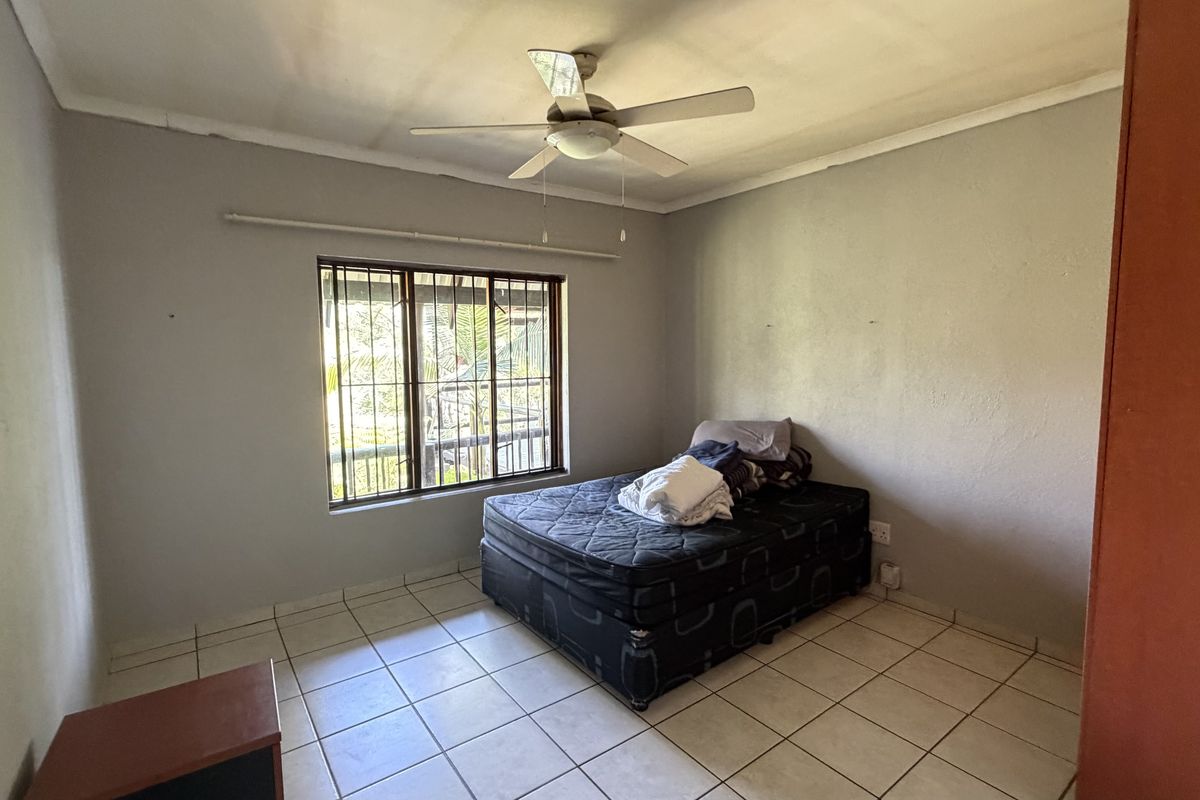 A bedroom featuring tiled flooring, a ceiling fan, and a window fitted with security bars.