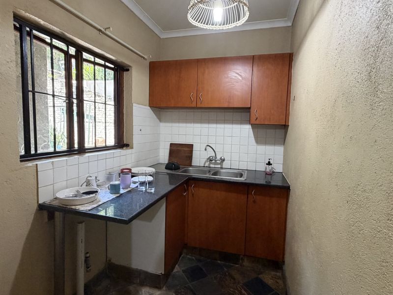 A compact kitchen featuring wooden cabinetry, granite countertops, a double sink, and tiled backsplash, offering a functional prep area with natural light.