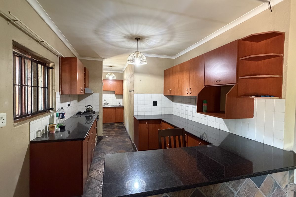 Functional kitchen featuring granite countertops, ample wooden cabinetry, tiled backsplash, and a gas hob, offering a practical layout for daily meal preparation.
