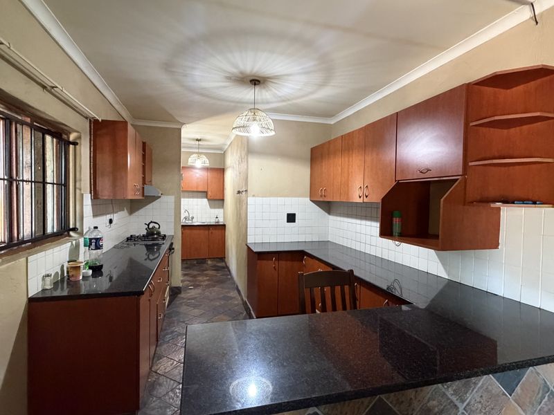 Functional kitchen featuring granite countertops, ample wooden cabinetry, tiled backsplash, and a gas hob, offering a practical layout for daily meal preparation.