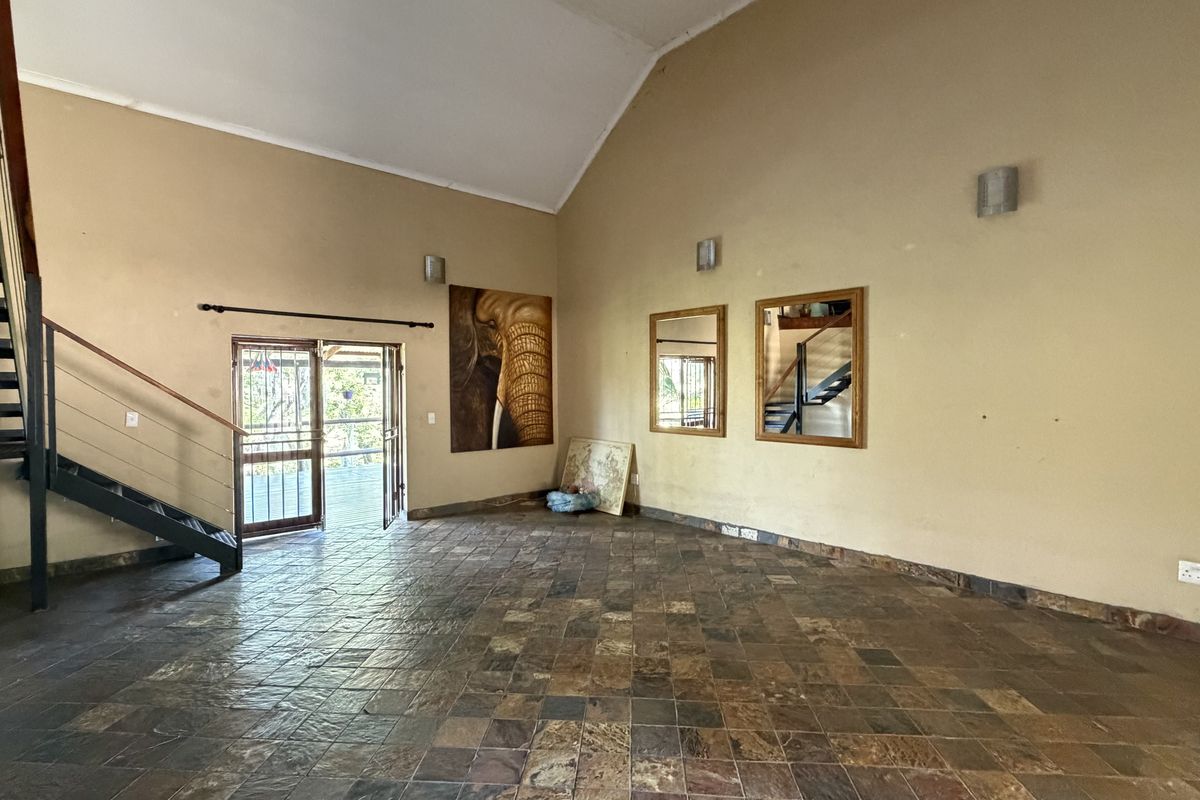 Spacious living area featuring vaulted ceilings, slate tile flooring, and a prominent metal staircase leading to an upper level.