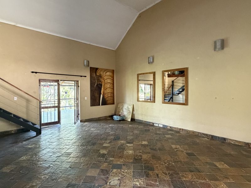 Spacious living area featuring vaulted ceilings, slate tile flooring, and a prominent metal staircase leading to an upper level.