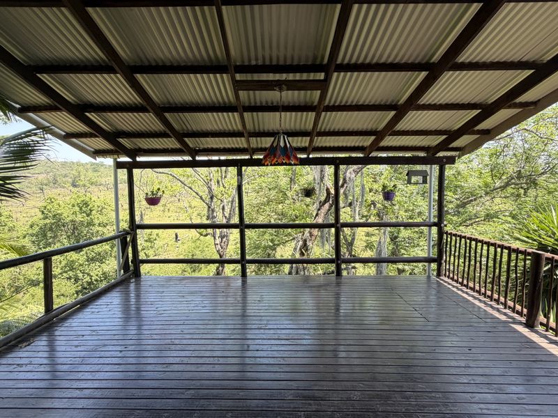 A spacious covered timber deck featuring a corrugated roof and wooden railings, offering an open-air space with scenic views of the surrounding landscape.