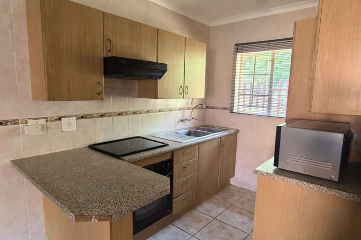 A functional kitchen featuring laminate cabinetry, granite countertops, built-in oven, electric hob, and tiled backsplash with a window for natural light.