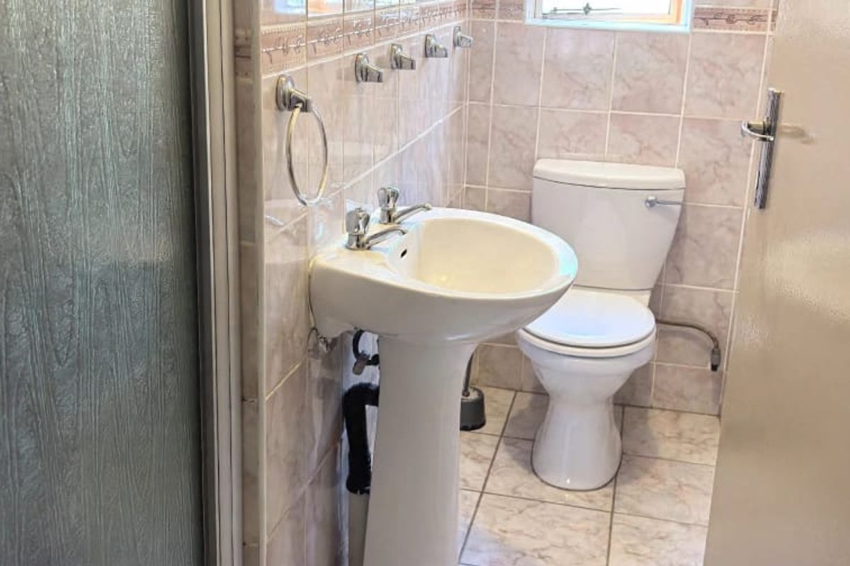 A functional bathroom featuring a pedestal basin, toilet, and shower enclosure with neutral ceramic wall and floor tiling.
