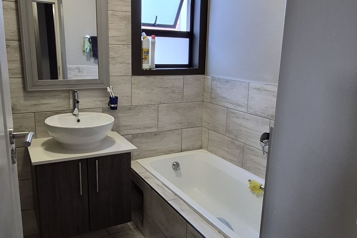 A well-maintained bathroom featuring a modern vessel sink, vanity cabinet, built-in bathtub, and contemporary wood-look tiled walls and flooring.