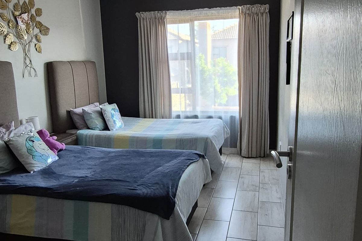 A well-maintained bedroom featuring light-toned tiled flooring, a neutral color palette, and a large window that allows for natural light.