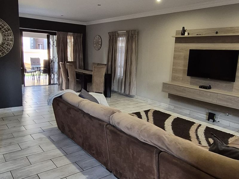 Spacious open-plan living and dining area featuring modern tiled flooring, recessed lighting, and a built-in media unit with direct access to the patio.
