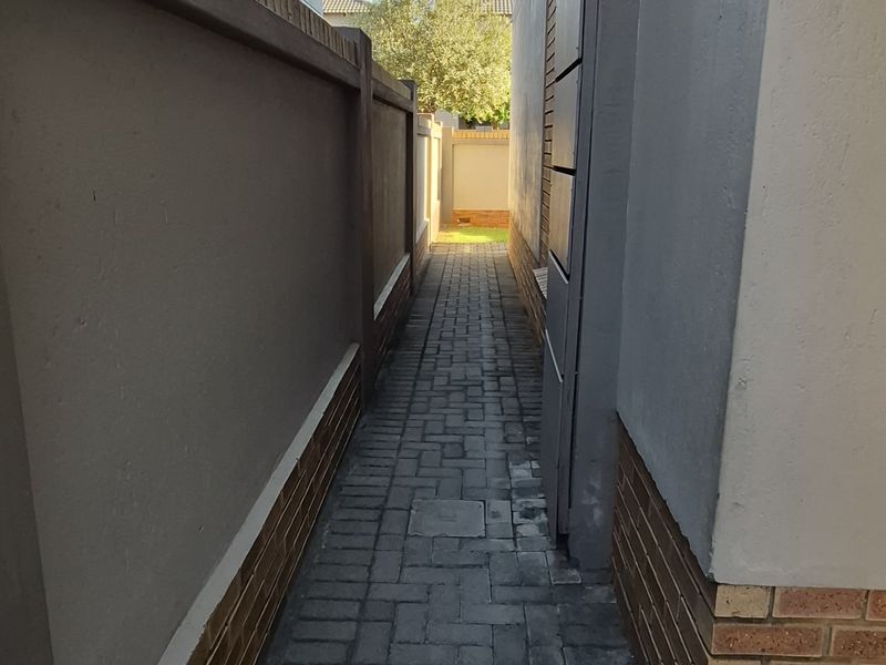 A narrow paved side walkway between two townhouse structures, featuring clean brickwork and boundary walling.