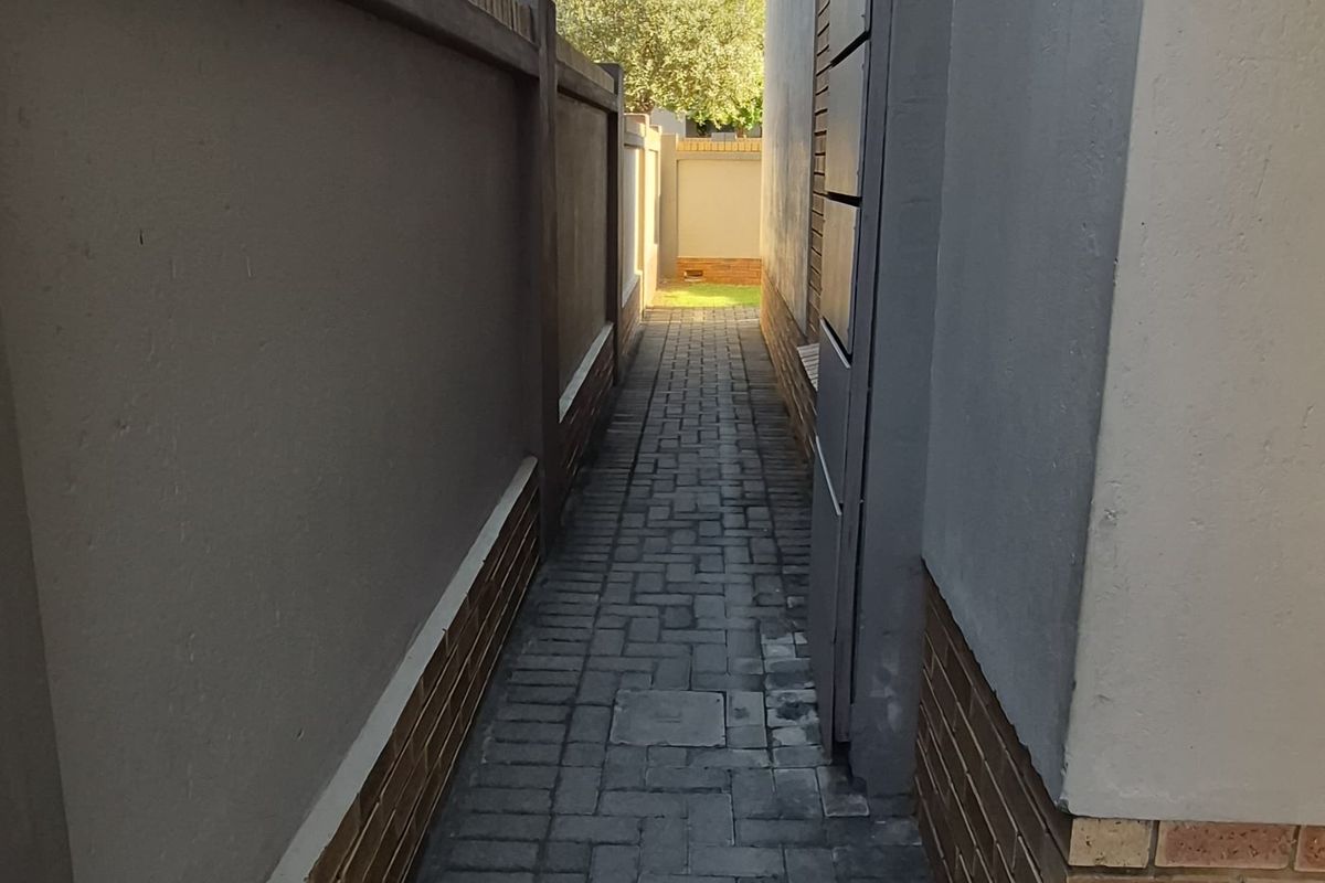 A narrow paved side walkway between two townhouse structures, featuring clean brickwork and boundary walling.