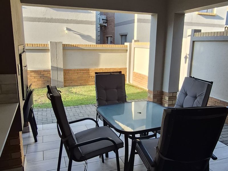 A covered patio area featuring tiled flooring and a built-in braai, providing a functional outdoor space for entertaining.