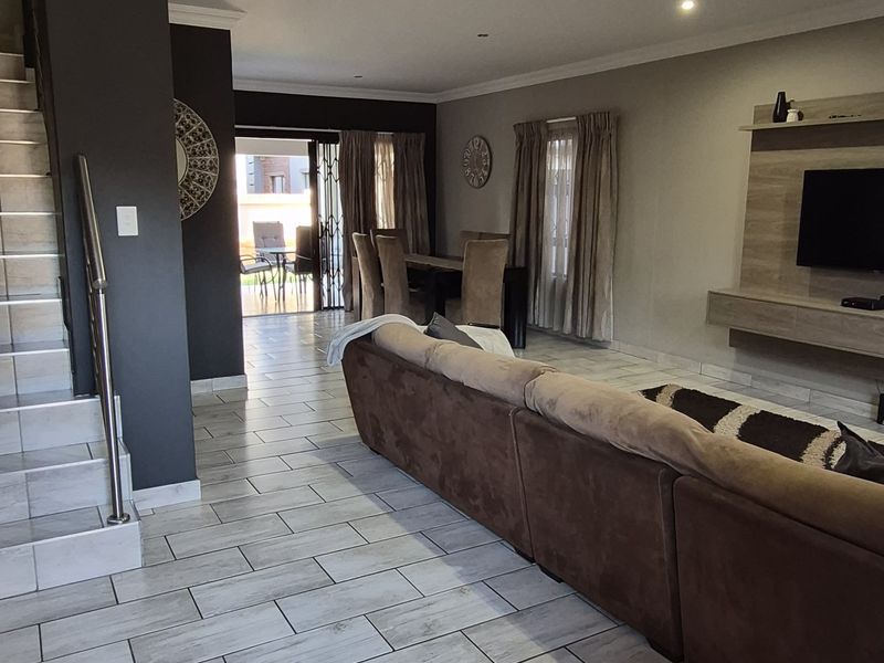 Spacious open-plan living and dining area featuring modern tiled flooring, recessed lighting, a built-in media console, and direct access to an outdoor patio.