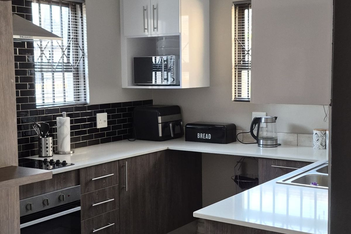 Modern kitchen featuring dark wood-grain cabinetry, white stone countertops, a tiled backsplash, built-in oven, and hob with contemporary tiled flooring.