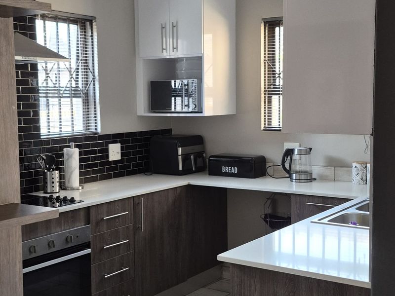 Modern kitchen featuring dark wood-grain cabinetry, white stone countertops, a tiled backsplash, built-in oven, and hob with contemporary tiled flooring.
