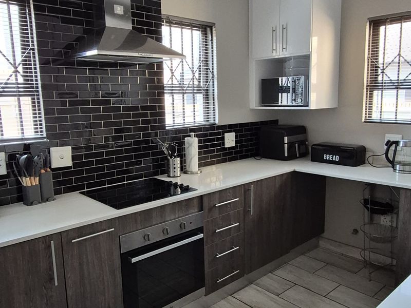 Modern kitchen featuring dark wood cabinetry, contrasting white upper cabinets, stone countertops, a sleek black tiled backsplash, and integrated stainless steel appliances.