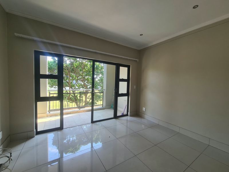 A bright, empty living room featuring polished tile floors, recessed lighting, and large sliding glass doors that open onto a private balcony.