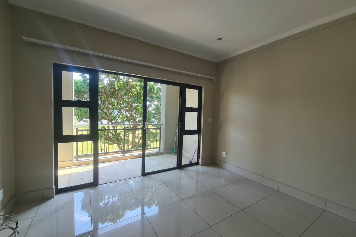 A bright, empty living room featuring polished tile floors, recessed lighting, and large sliding glass doors that open onto a private balcony.