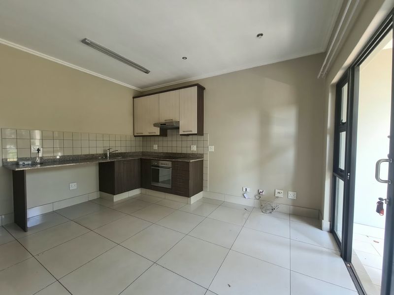 An open-plan kitchen area featuring modern built-in cabinetry, granite countertops, integrated oven, and tiled flooring, with direct access to an outdoor patio.