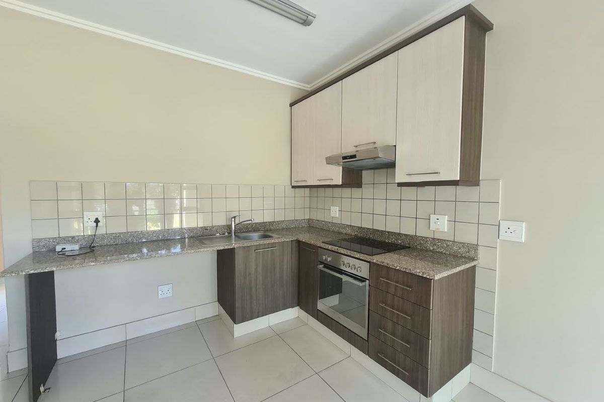 A clean and functional kitchen featuring granite countertops, built-in oven, electric hob, extractor fan, and ample cabinetry with neutral tiled finishes.