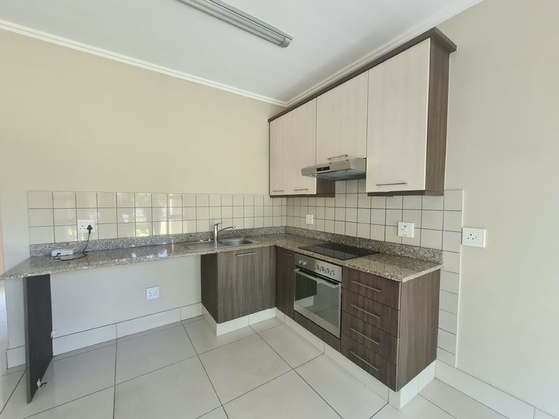 A clean and functional kitchen featuring granite countertops, built-in oven, electric hob, extractor fan, and ample cabinetry with neutral tiled finishes.