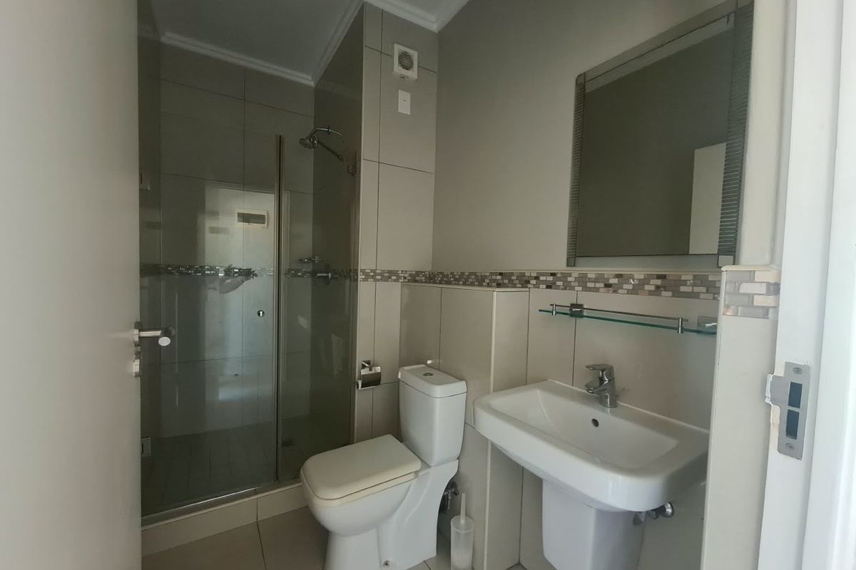 A clean, modern bathroom featuring a glass-enclosed shower, wall-mounted basin, and neutral tiled finishes throughout.