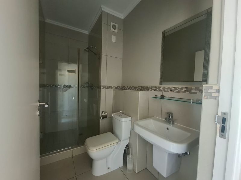 A clean, modern bathroom featuring a glass-enclosed shower, wall-mounted basin, and neutral tiled finishes throughout.