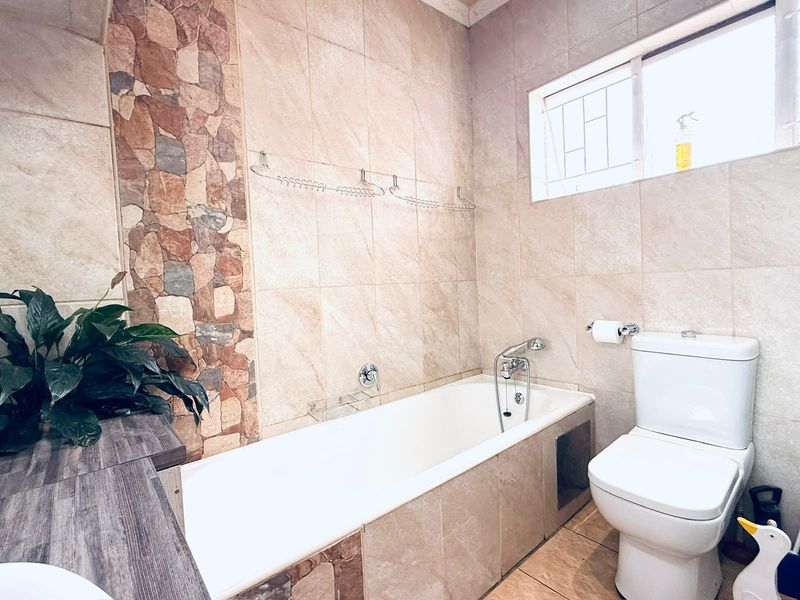 A well-maintained bathroom featuring a bathtub, toilet, and decorative stone accent wall with neutral tiling throughout.