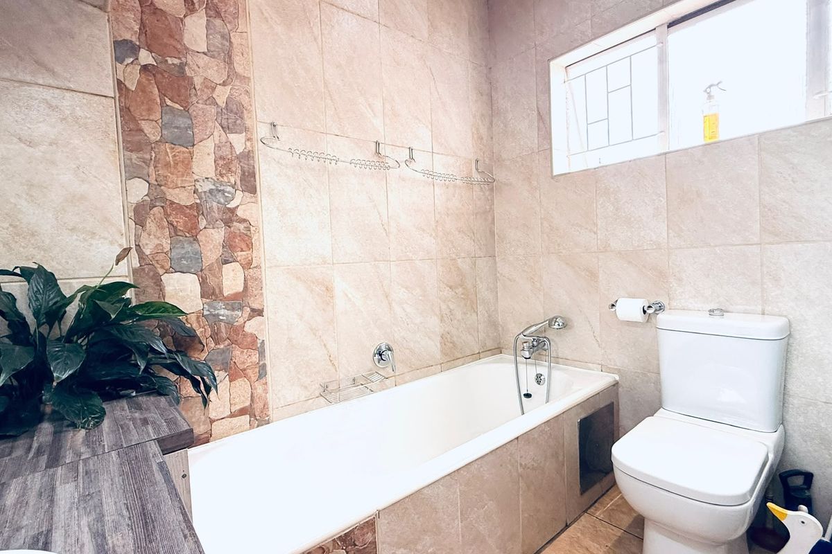 A well-maintained bathroom featuring a bathtub, toilet, and decorative stone accent wall with neutral tiling throughout.
